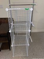Photo showing the full white wire mesh storage unit with three cube shelves vertically stacked, with plastic corner connectors, placed indoors on a floor near a wall.