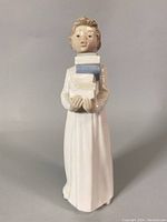 Front view of the NAO porcelain figurine showing the girl holding books in a long white dress.