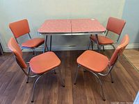 Five-piece retro kitchen set with pink Formica table and vinyl chairs viewed from angle showing the full set.
