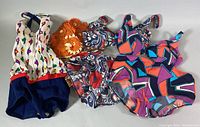 Four pieces display: two one-piece swimsuits, two-piece bikini, orange swim cap, laid flat to show patterns and colors