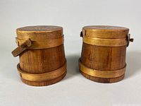 Front angle view showing two small staved pine wood flour barrels, one slightly darker wood tone than the other, with wooden hoops and side knots but no handles.