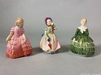 Front view of three Royal Doulton figurines in pink, pastel, and green dresses