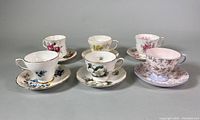 Five bone china teacups with matching saucers, floral patterns, arranged side by side.