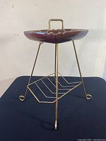 Ashtray on metal stand showing front angle, brown ceramic with green corners and gold handle, metal stand geometric style with curled leg feet.