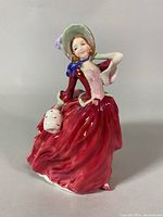 Front view of Royal Doulton Autumn Breezes porcelain figurine showing full figure in red dress and bonnet holding a muff.