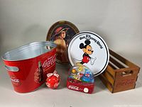 Photo shows entire lot including Coca-Cola party tub, wooden crate, Mickey Mouse tin tray, vintage portrait tray, Coca-Cola snow globe, and red ornament.