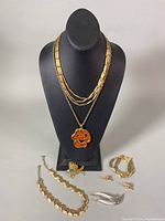 Full lot arranged on display bust and tabletop showing all items: multiple necklaces displayed on bust stand and brooches, bracelet, earrings on table.