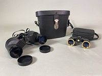 Photo shows Tasco J-B208 opera glasses and Eatons 7x35 binoculars with their respective carrying cases on a flat surface. Both optical devices have minor surface wear.