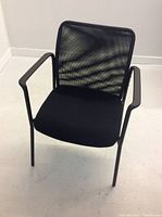 Front view of a single black office chair showing the mesh back, cushioned seat, and straight black metal legs with armrests.