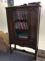 Front view of tall antique dark oak cabinet with glass door, containing books and papers inside. Shows overall shape, size and finish.