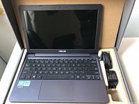 Open ASUS VivoBook laptop inside original box with charger and cable visible