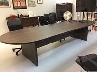 Full view of the large dark wood boardroom table with four office chairs around it in an office setting.