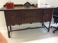 Front view of antique dark oak credenza showing two side cabinets and three central drawers with wooden knobs.