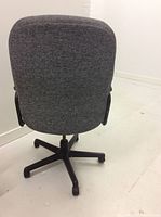 Back view of tall grey cushioned office chair showing full back and black swivel base with wheels.