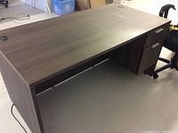 View of the entire dark brown desk showing flat top surface, two drawers on the right, and cable passthrough hole on the left.