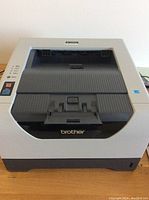 Top and front view of Brother HL-5370DW printer showing feed tray, control buttons, and Brother branding.