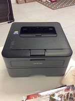 Front and top view of black Brother HL-L23200D printer on a light surface.