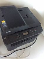 Full view of Brother DCP-7065DN printer showing paper tray, control panel, and wired connections.