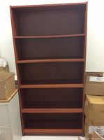 Front view of the red wooden bookshelf showing its five shelves and the red wood grain finish.