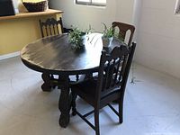 Photo of round oak dining table set with two wooden chairs, showing table leg detail and surrounding area.