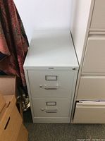 Grey metal filing cabinet with two drawers, viewed from front showing locked top drawer.