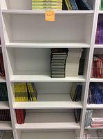 Front view of the white 7-tier bookshelf showing three middle shelves with some books on a few shelves and the rest of the shelves empty.