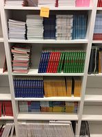 Full front view of the white 7-tier bookcase filled with books and binders for size reference, showing clean white shelves and solid construction.