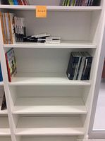 Photo shows four of the seven white shelves with some books and items on the shelves, indicating size and scale.