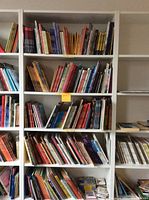 Front view of the tall white 7-tier bookshelf filled with various books to show shelf spacing and condition.