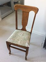 Front view of one wooden dining chair with worn leaf-patterned upholstered seat. Chair back shows carved design.