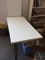 Photo showing white computer desk with metal legs, displayed in a room setting.