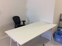 Wide white computer desk with black office chair in background showing the full desk surface and legs.