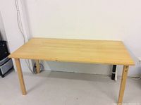 Full view of the rectangular light wood table showing three wooden legs and one black metal leg.