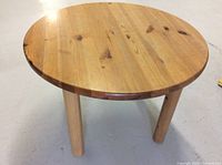 Round wooden side table showing full top and length of legs against neutral floor.