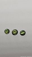 Three round green sapphires displayed on a flat surface showing their size and color.