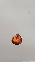 Top-down photo of a pear cut sapphire gemstone showing the deep orange color and faceted surface.