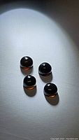 Four polished round cabochon stones with chocolate brown and black coloring, translucent and shiny under light, arranged in a group on a white surface.
