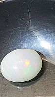 Oval cabochon cut Ethiopian opal gemstone on black background showing play of color in red, green, and orange hues.