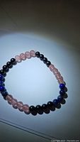 Stretchy bracelet made of alternating polished beads of strawberry quartz (pink), black onyx (black), and lapis lazuli (blue) arranged in sections on a flexible cord.