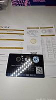 GRA Certificate document showing details of 5mm 0.5ct VVS1 D color moissanite grading, with authenticity card in front.