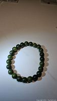 Photo of a circular stretchy bracelet composed of uniformly sized green jade beads around 10mm diameter on a white background.