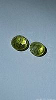 Two yellow-green sphene gemstones on dark fabric background showing color and cut details.