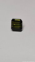 Front-facing image of green octagonal-cut tourmaline gemstone on white background showing its color and clarity.