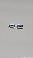 Two emerald cut sky blue topaz gemstones side by side on neutral background