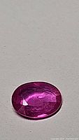 Close-up photo of an oval-shaped bubblegum pink natural sapphire gemstone with visible surface texture and inclusions.