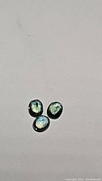Three oval faceted tri-colored sapphires on a white background showing blue, green, and yellow hues.