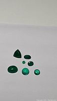 Seven vivid lime green onyx gemstones arranged on white background, varying shapes and sizes visible.