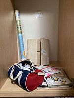 Full view of the shelf holding a rolled Olympic poster, a wooden hardcover book organizer, a duffle bag, and some folded clothes or textiles.