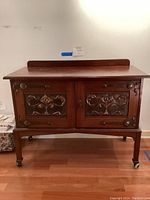 Front full view of the wooden cabinet with decorative metal door panels close up showing symmetrical metal floral and scroll pattern and wood framing.