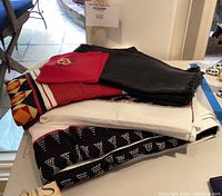 Photo of folded black placemats with fringe edges, folded white tablecloth, black and white dotted pattern table runner, red napkins with embroidered flowers, and a multicolor geometric item.